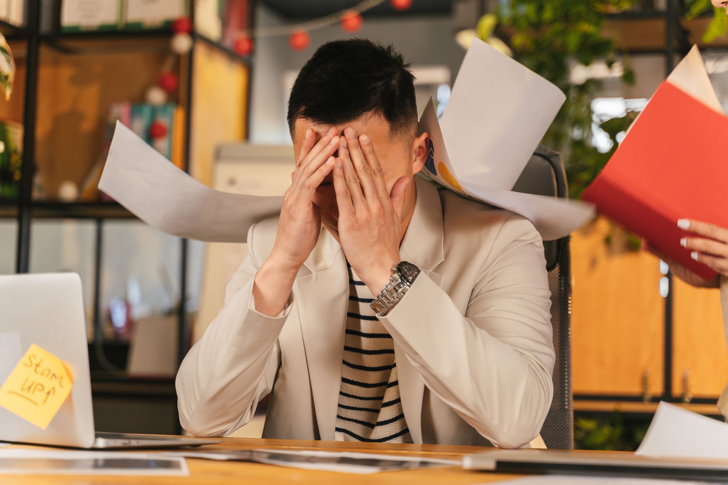 An overwhelmed business owner surrounded by scattered paperwork and sticky notes